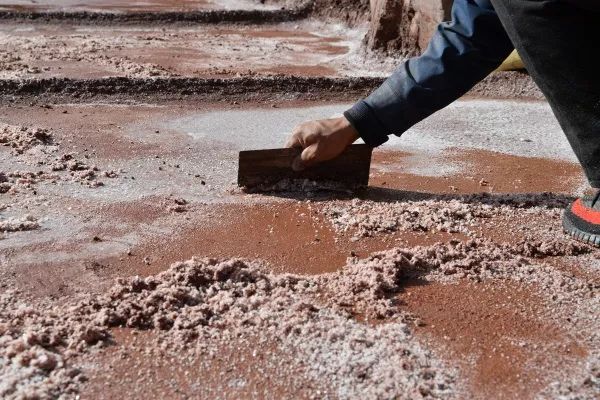 盐田卤水风干成盐,盐民用工具轻轻刮取盐结晶